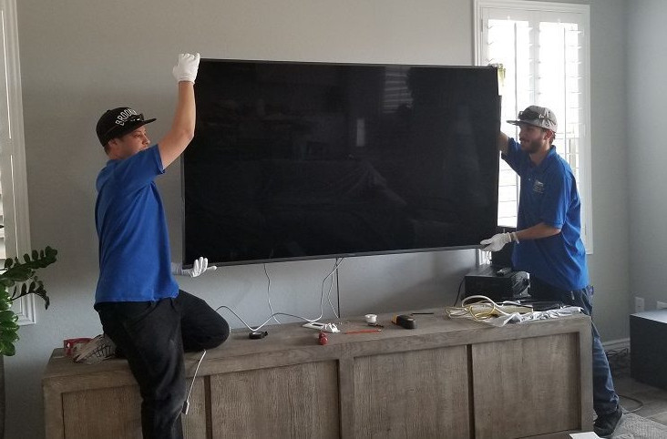 Two technicians mounting TV on to an interior wall.